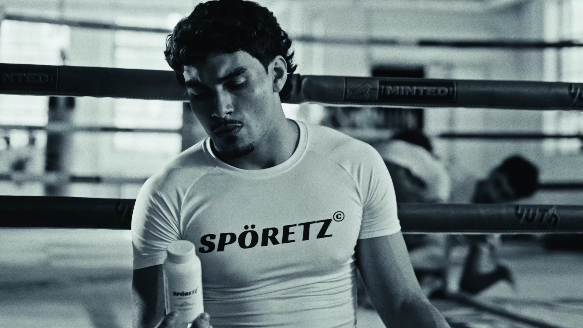 Boxer in a white Spöretz shirt holding the MB40 probiotic bottle ringside, black-and-white photo